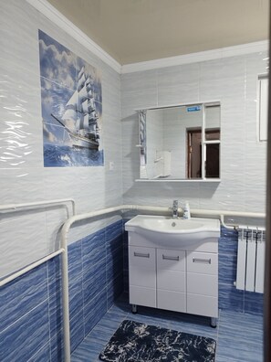 A bathroom with a white sink, a mirror, and a blue-tiled wall. - Travel Around Guest House (Kochkor)