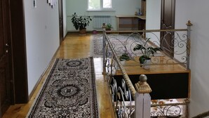 A spacious hallway with a patterned carpet, a staircase with ornate metal railings, and a ceiling with a radiant light fixture. - Travel Around Guest House (Kochkor)