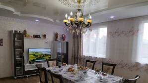A dining room with a chandelier, a television, and a floral tablecloth. - Travel Around Guest House (Kochkor)