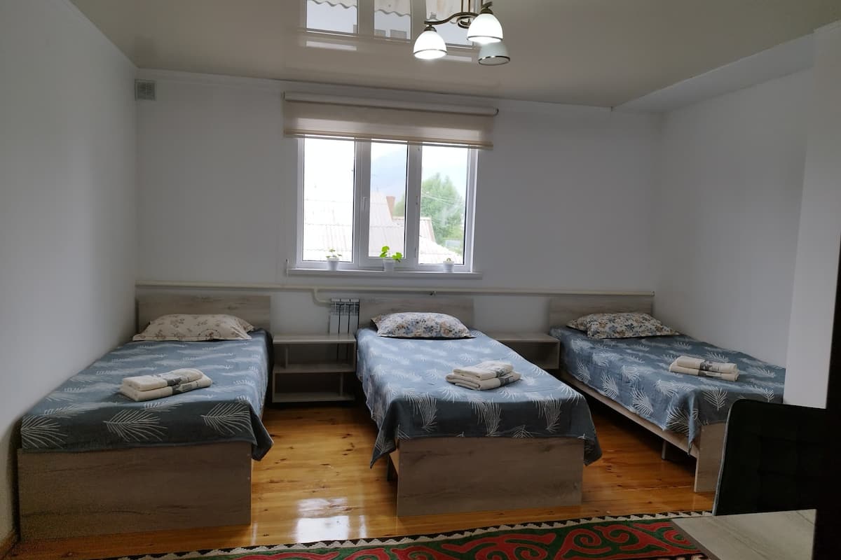 A room with three beds, a window with blinds, a ceiling fan, and a patterned rug.
