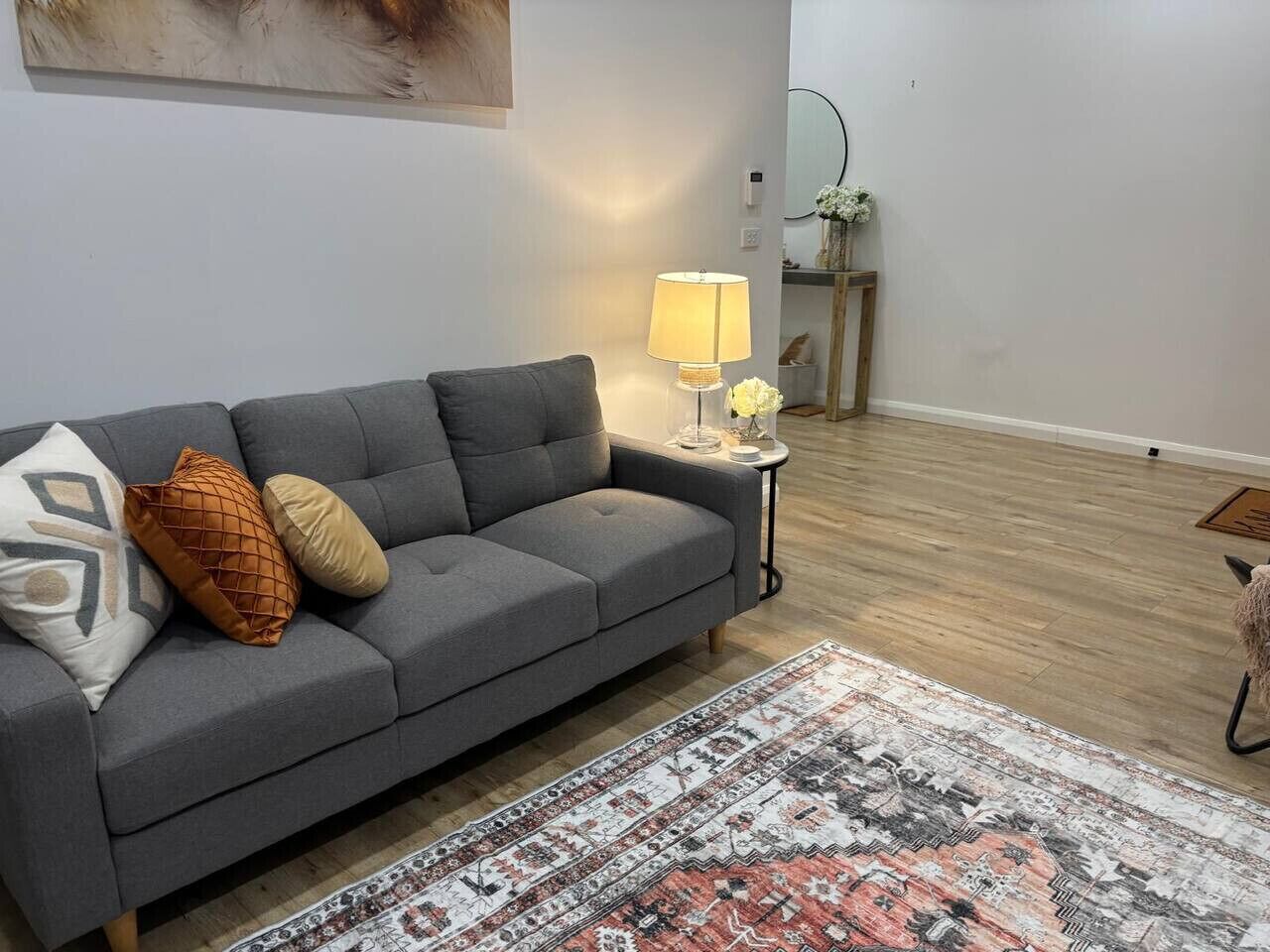 Un salon avec un canapé gris, un tapis à motifs et une table d’appoint sur laquelle se trouve une lampe.