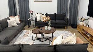 Ein modernes Wohnzimmer mit einer Sofagarnitur, einem Couchtisch und einem Fernseher auf einem Holzständer.