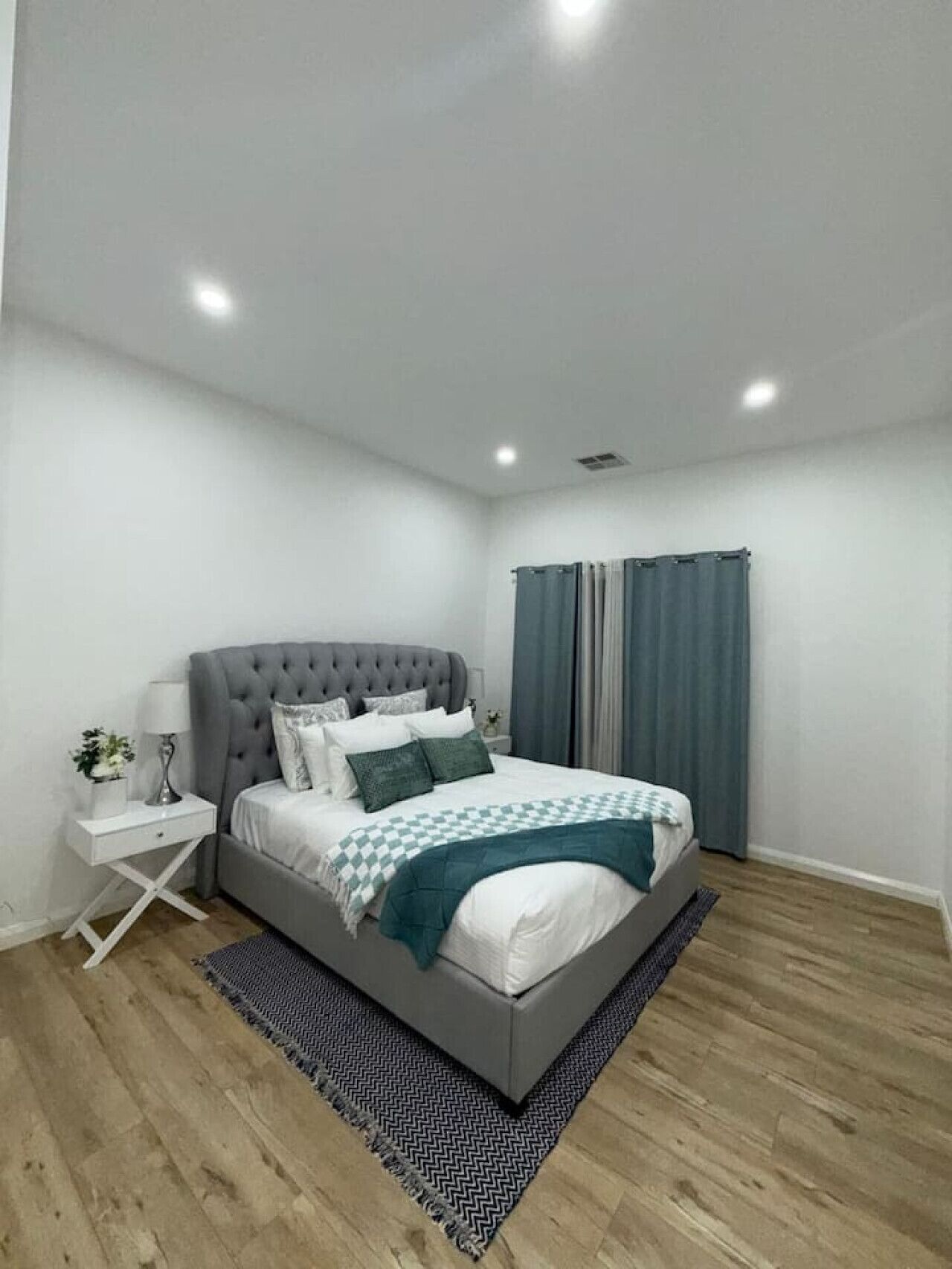 Un dormitorio moderno con una cama tapizada en gris, ropa de cama blanca y una manta a cuadros.