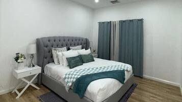 Un dormitorio moderno con una cama tapizada en gris, ropa de cama blanca y una manta a cuadros.