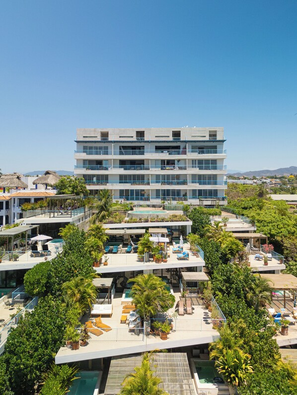 Un hôtel à plusieurs étages doté de piscines extérieures, de balcons et d’une végétation luxuriante.