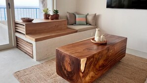 A modern living room with a wooden coffee table, a sofa with cushions, a TV mounted on the wall, and a view of the sea through large windows. - Oceanfront 2-bedroom luxury at La Escondida - Relax & Enjoy! (Puerto Escondido)