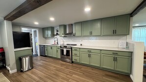 Une cuisine spacieuse avec des meubles de couleur vert clair, un réfrigérateur en acier inoxydable et un plancher en bois.