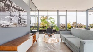 A modern living room with a sofa, a coffee table, and a chair. There is a large window with a view of greenery outside. - Cozy & beautiful place in downtown in CDMX D6 (Ciudad de México)