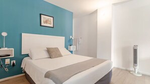 A modern bedroom with a large bed, a bedside table, a wall-mounted light, and a standing fan. - Cozy & beautiful place in downtown in CDMX D6 (Ciudad de México)