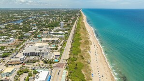 An aerial view of a coastal city with a long beachfront, a river running parallel to the beach, and a mix of residential and commercial buildings.