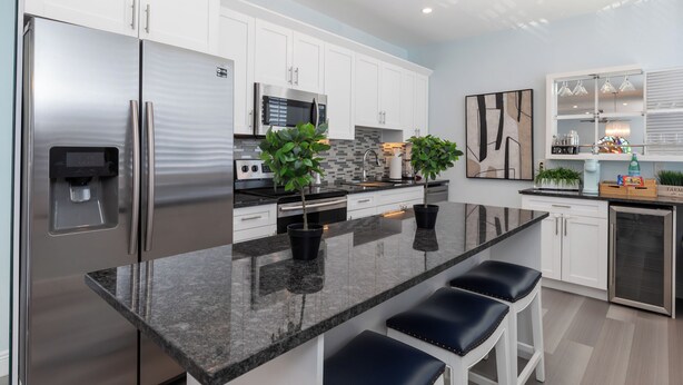 A modern kitchen with white cabinets, stainless steel appliances, a granite countertop, and bar stools.