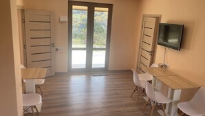 A room with a wooden floor, a sliding door with a view, a TV mounted on the wall, and a table with chairs. - Lovely 5-bedroom house with WiFi in charming Dilijan (Dilijan)