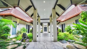 A covered walkway with a tiled roof, surrounded by lush greenery and a stone pathway.