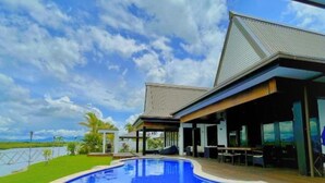 A modern building with a swimming pool, covered patio, and a view of the water. - Four Bedroom Riverfront Villa 62 (Nadi)