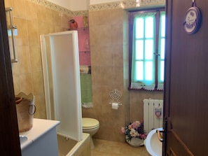Une salle de bain avec une douche, des toilettes et un lavabo. Il y a une fenêtre avec un rideau, et un hibou décoratif est accroché au mur.