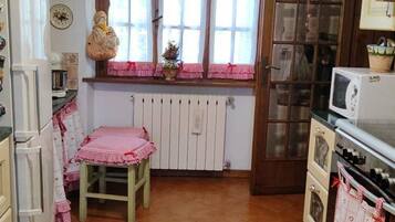 Una cocina con piso de baldosas, un taburete de madera, un refrigerador, un microondas y una ventana con cortinas.