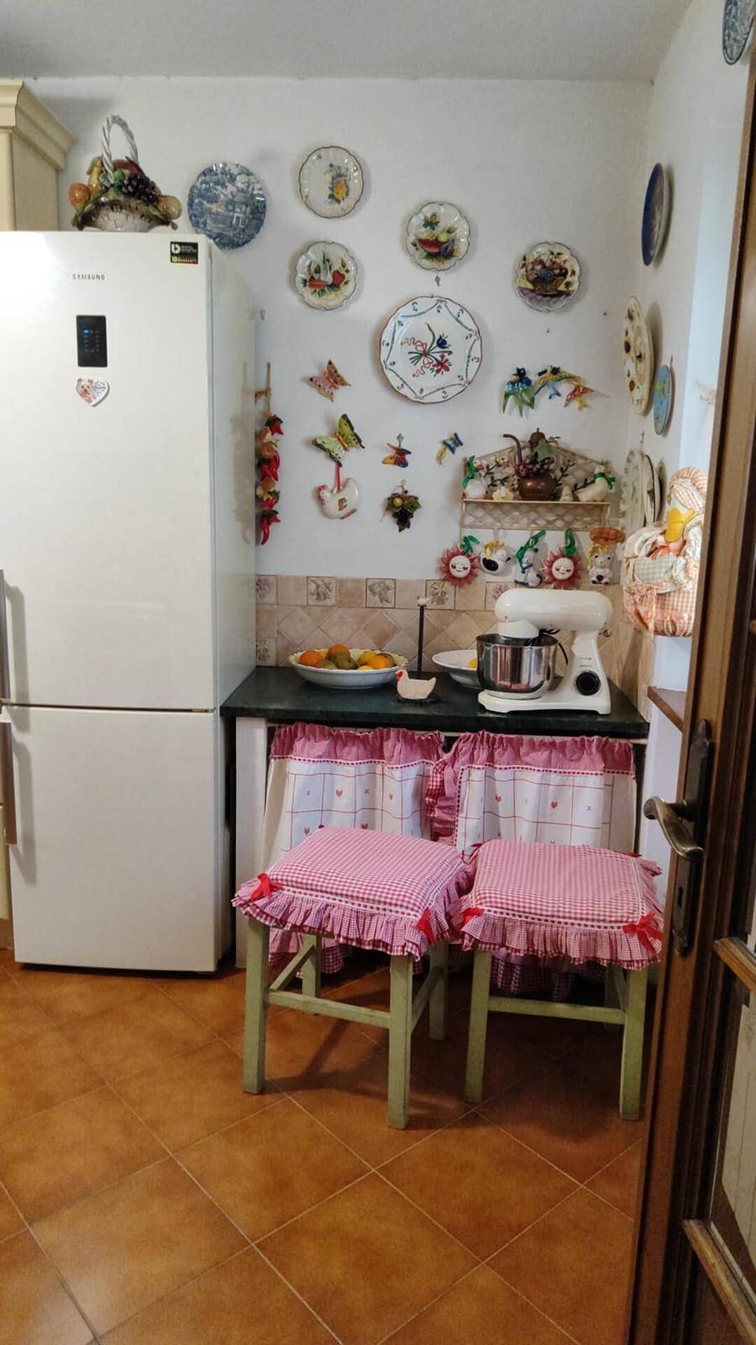 Una cocina compacta con un refrigerador blanco, una mesita con mantel a cuadros y varios platos decorativos en la pared.