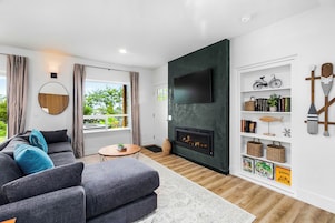 Una sala de estar moderna con un sofá gris, un espejo redondo, una chimenea y una estantería con diversos objetos.