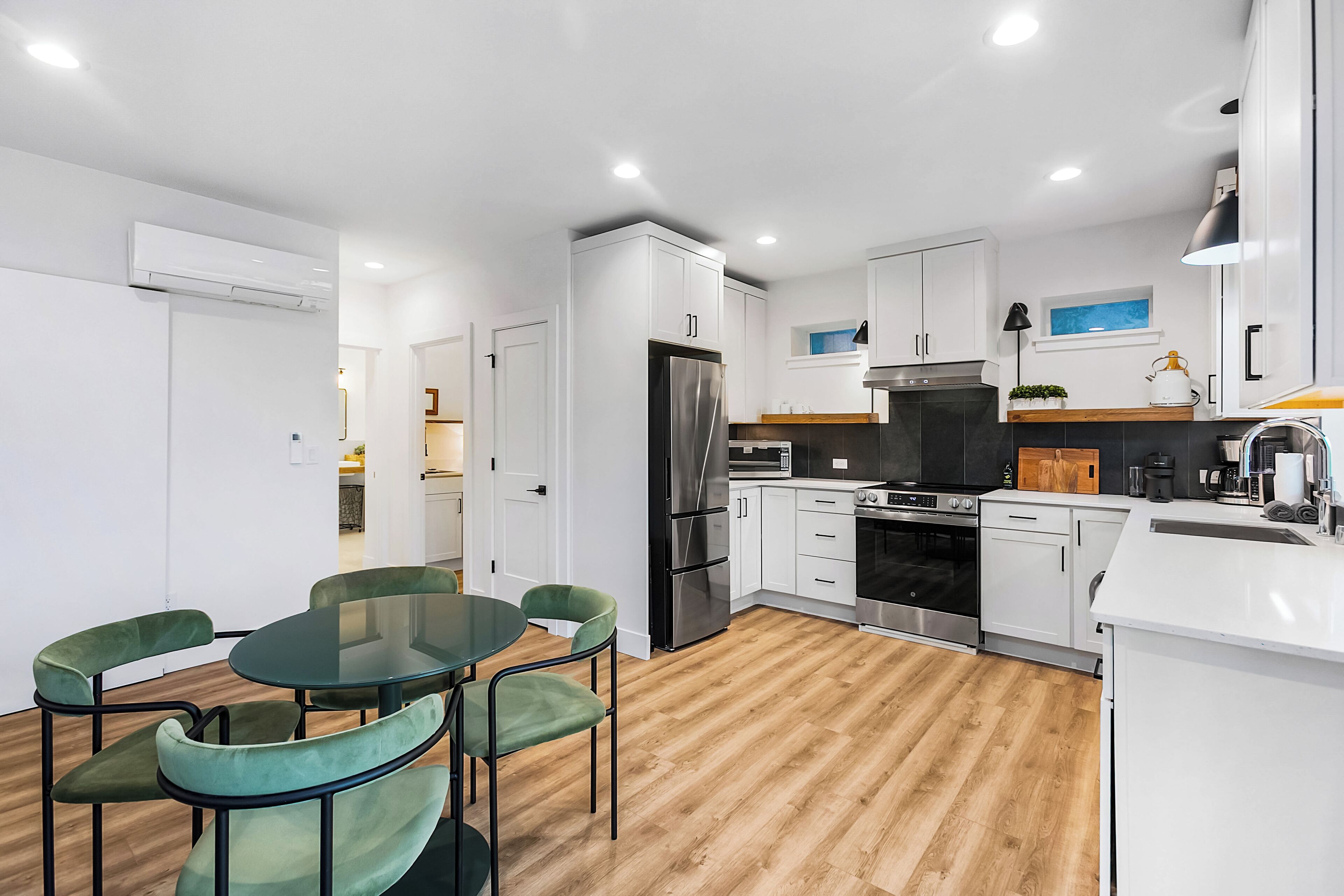 A modern kitchen with white cabinets, a stainless steel refrigerator, and a dining area with green chairs.