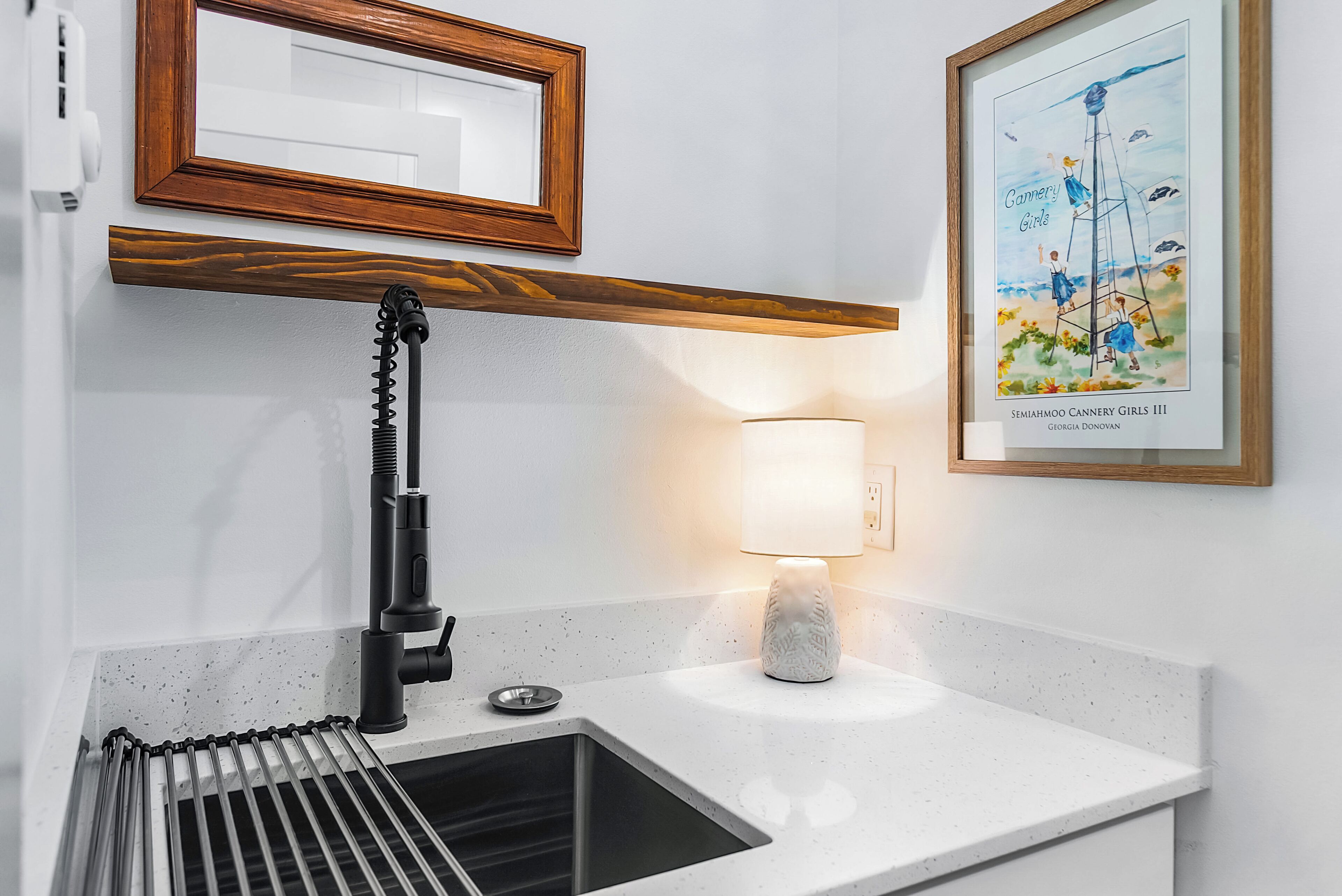 Una cocina con un grifo moderno, un lavabo, una encimera, un cuadro enmarcado y una lámpara fijada a la pared.