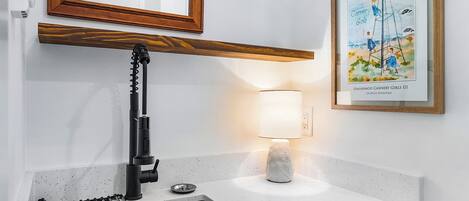 Une cuisine équipée d’un robinet moderne, d’un évier, d’un plan de travail, d’un tableau encadré et d’un luminaire fixé au mur.