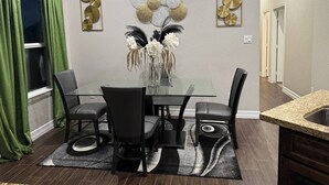 Een eetgedeelte met een glazen tafel, zwarte stoelen, een decoratieve vaas en abstracte wanddecoratie.