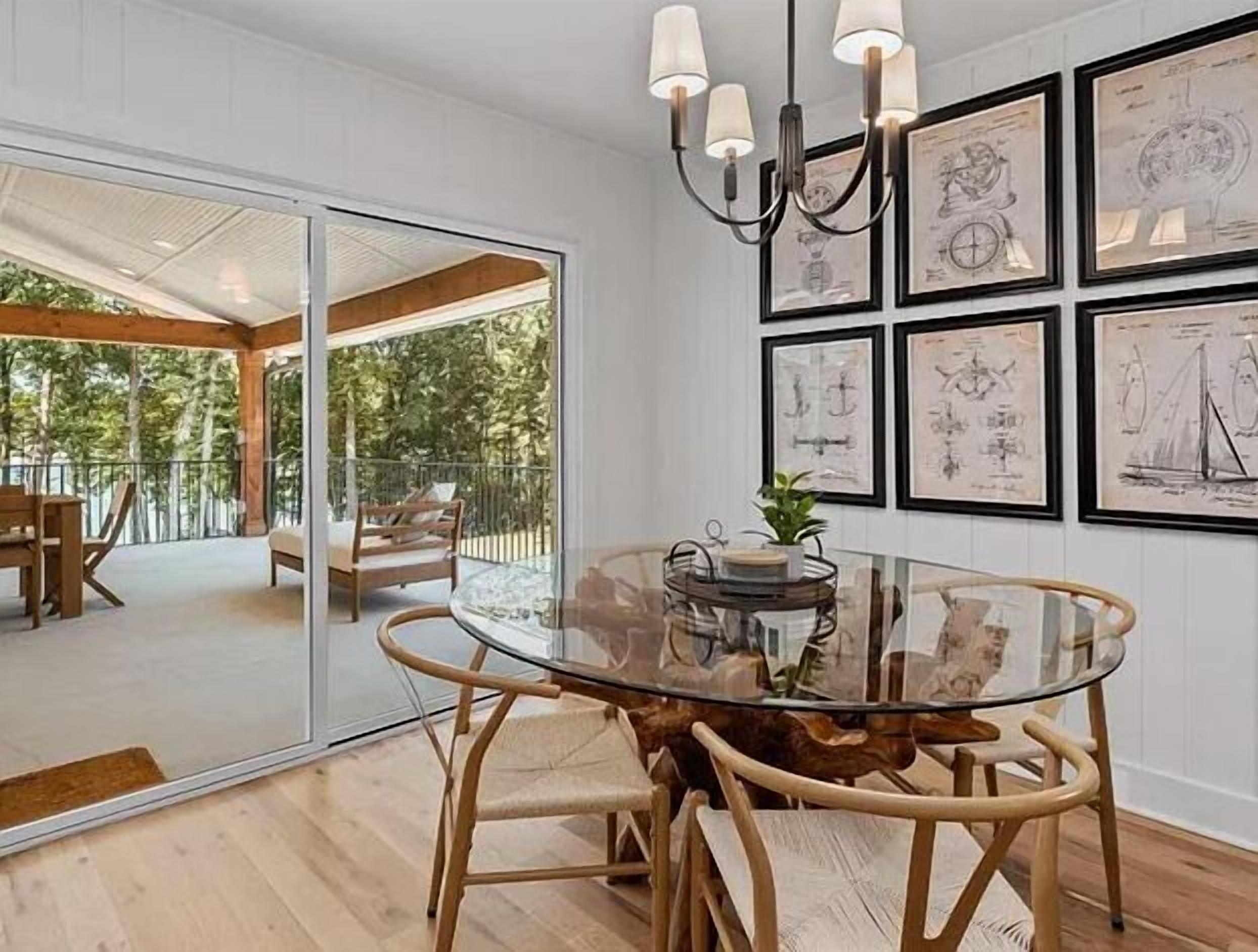 A dining area with a glass table surrounded by wooden chairs, a chandelier, and framed nautical illustrations on the wall.
