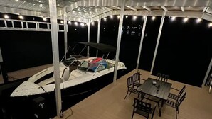 A covered outdoor area with a boat docked under a canopy, a table with chairs, and a view of the water. - Lake Lanier Luxury Water Front Retreat with Large Dock, Boat Rental & Lake Views (Buford)