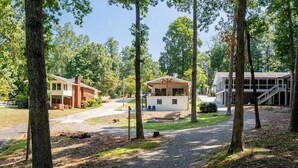 A lodge with a central building surrounded by trees, a gravel path, and a small dock. - Lake Lanier Luxury Water Front Retreat with Large Dock, Boat Rental & Lake Views (Buford)
