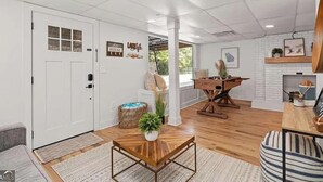 A spacious living area with a wooden coffee table, a sofa, and a foosball table. There is a door with a window, a wall-mounted shelf, and a basket on the floor. - Lake Lanier Luxury Water Front Retreat with Large Dock, Boat Rental & Lake Views (Buford)