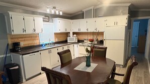 A modern kitchen with white cabinets, a dining table with chairs, and a microwave.