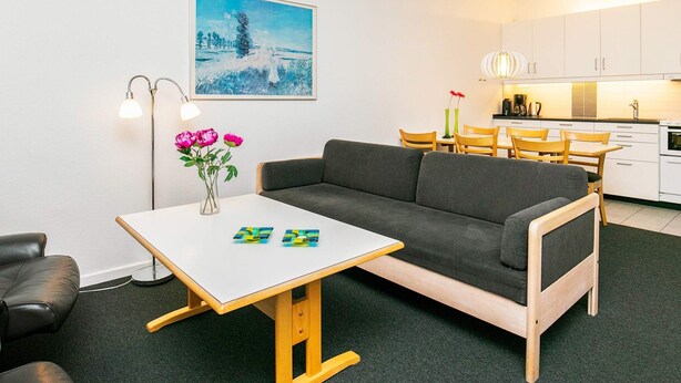 A modern living room with a gray sofa, a small white table with a vase of flowers, and a painting of a snowy landscape. - 4 Person Holiday Home on a Holiday Park in Faaborg (Faaborg)