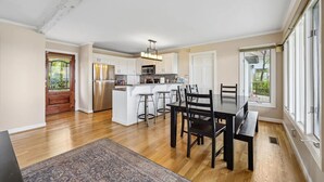 A spacious kitchen with a central island, a dining area with a table and chairs, and large windows offering a view of the outdoors.