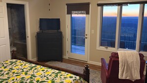 A bedroom with a bed, a ceiling fan, a dresser, a chair, and a balcony with a view.