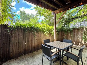 Patio esterno con tavolo e sedie in legno, recinzione di legno e luci a stringa.