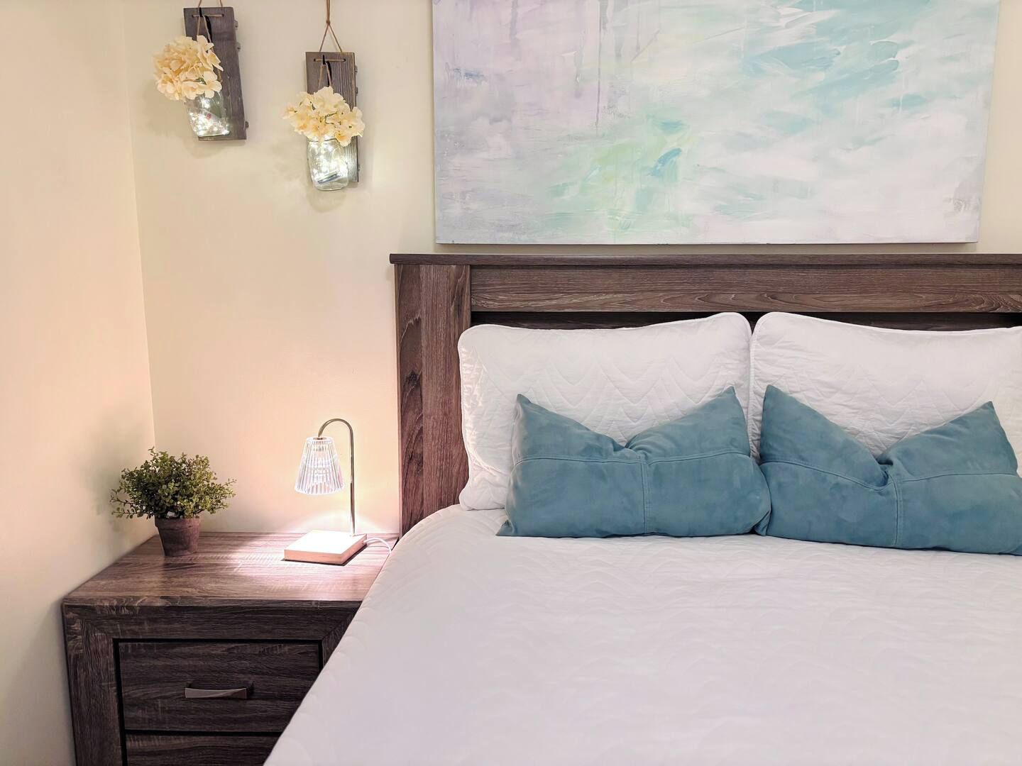 A bedroom with a wooden headboard, a bedside table with a lamp, and a wall-mounted flower arrangement.