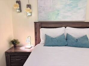 Una camera da letto con una testiera in legno, un comodino con una lampada e un vaso di fiori fissato alla parete.