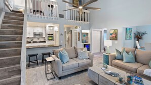 A spacious living area with a high ceiling, a staircase, and a kitchen area.