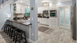 A modern kitchen with white cabinets, stainless steel appliances, and a bar area with stools.