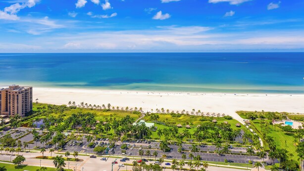 A coastal resort with a beachfront, parking area, and lush greenery.