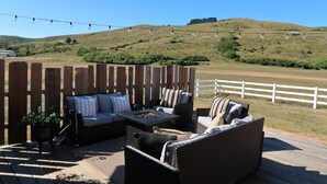 Une terrasse extérieure aménagée avec des meubles en osier, un foyer et une vue sur un paysage vallonné.