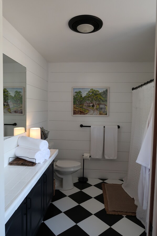 A bathroom with a black and white checkered floor, a white toilet, a sink with a mirror, and a painting on the wall.