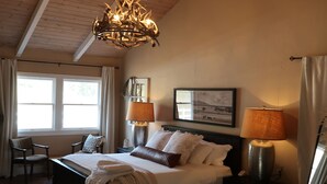 Une chambre avec un plafond en bois, un lit avec deux lampes, un tapis en peau de vache et une fenêtre avec des rideaux.
