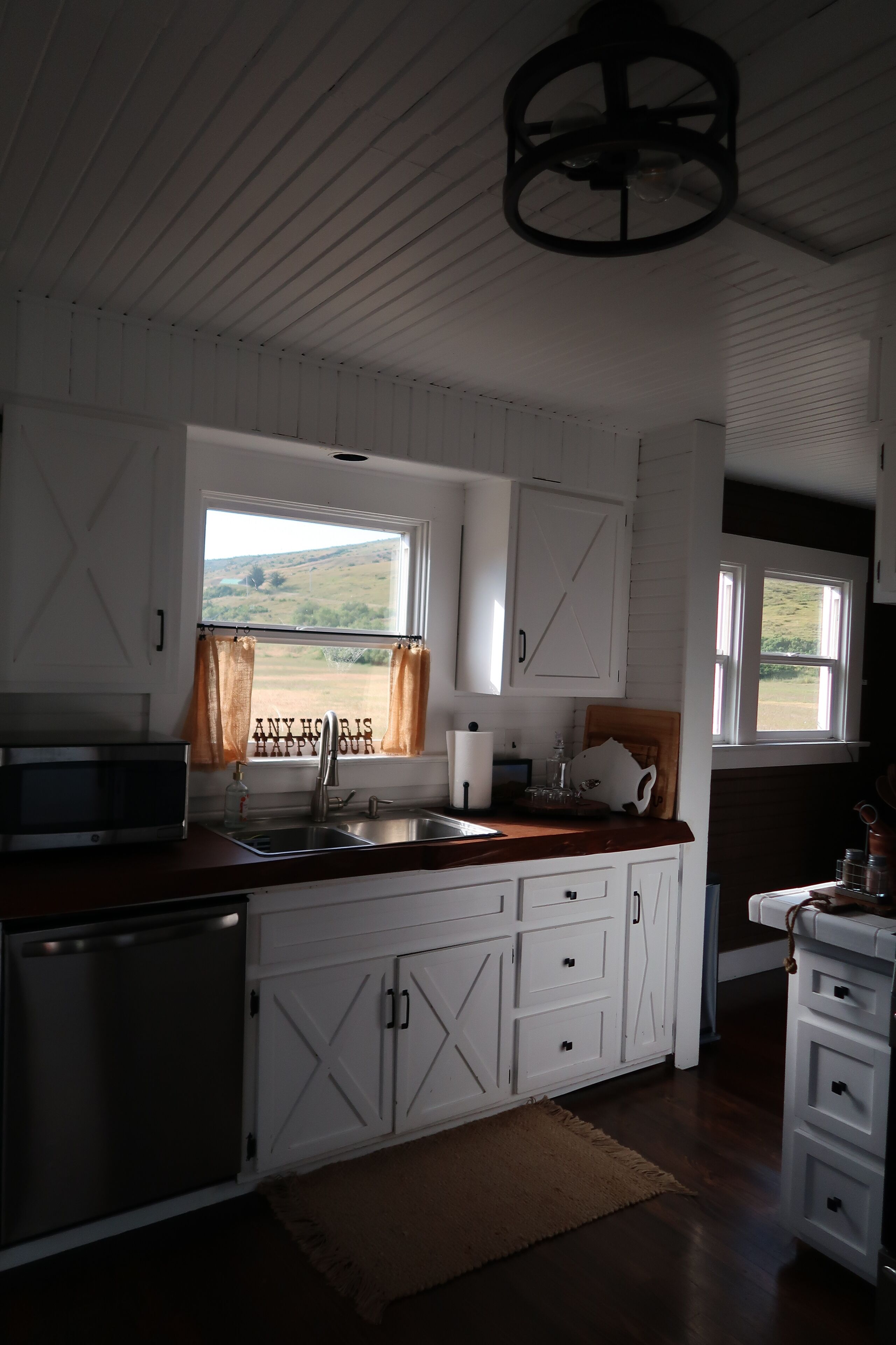 A kitchen with white cabinetry, a wooden countertop, a sink, a stove, and a window with curtains.