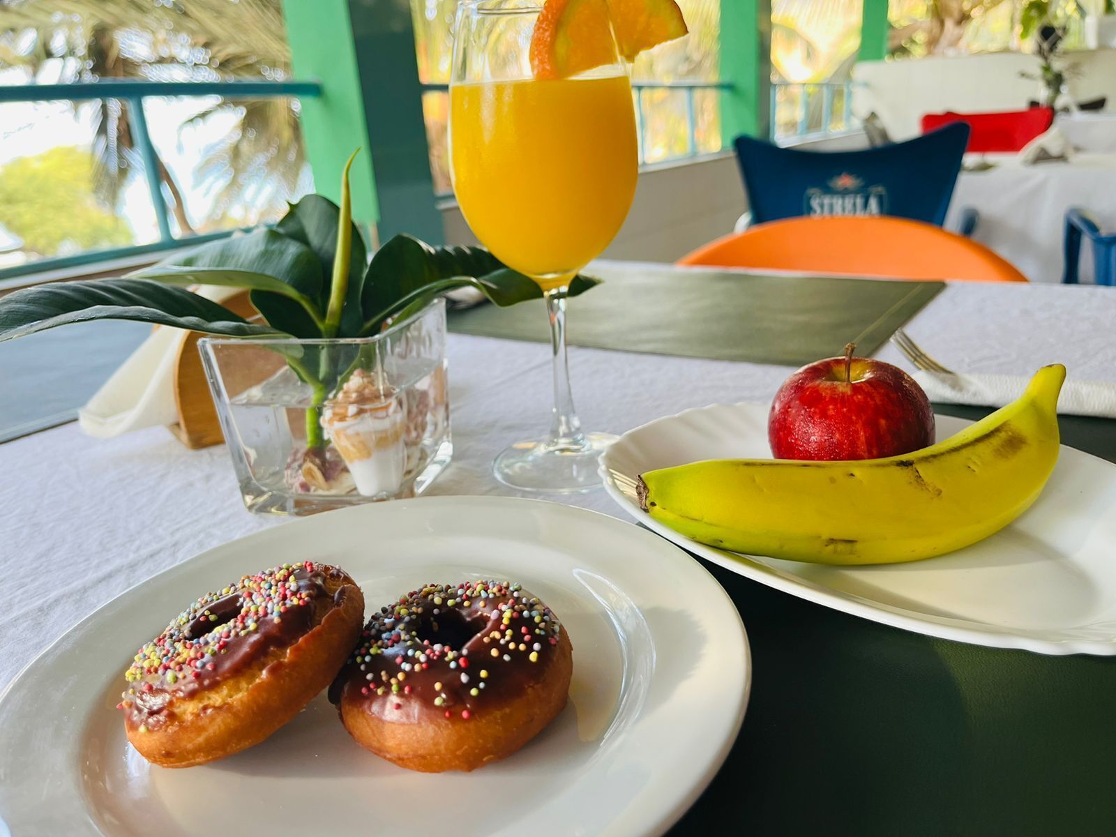 A table with a plate of donuts, a banana, an apple, and a glass of orange juice.