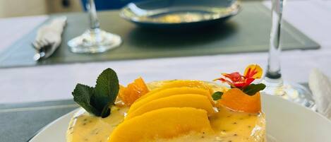 Un dessert présenté sur une assiette, composé d’une tranche de mangue et de quelques fleurs, accompagné de deux verres d’eau.
