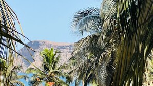A tropical resort with palm trees, a beach view, and a mountain in the background. - Hotel Village Penareia (Tarrafal)