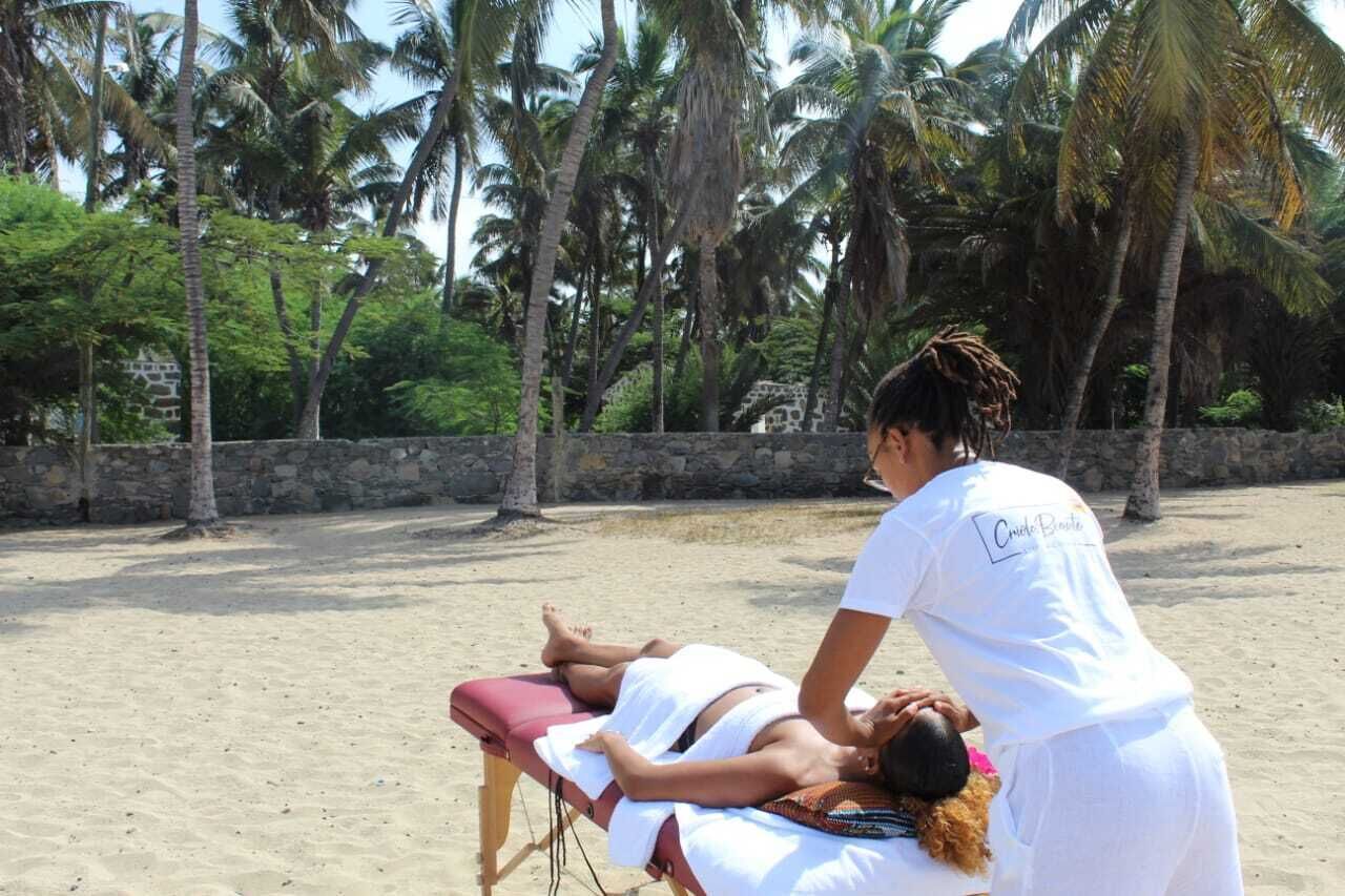 A massage therapy session on a sandy beach with palm trees in the background.