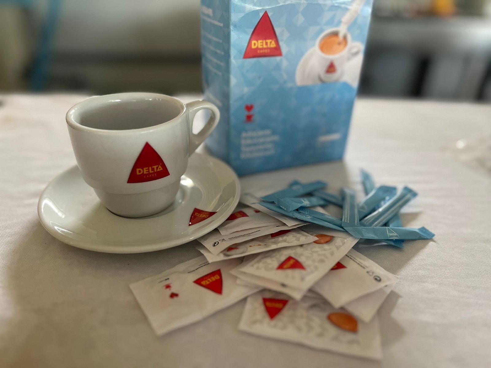 Een kopje en schoteltje met een Delta logo, een doos Delta koffie en losse koffiehoezen.