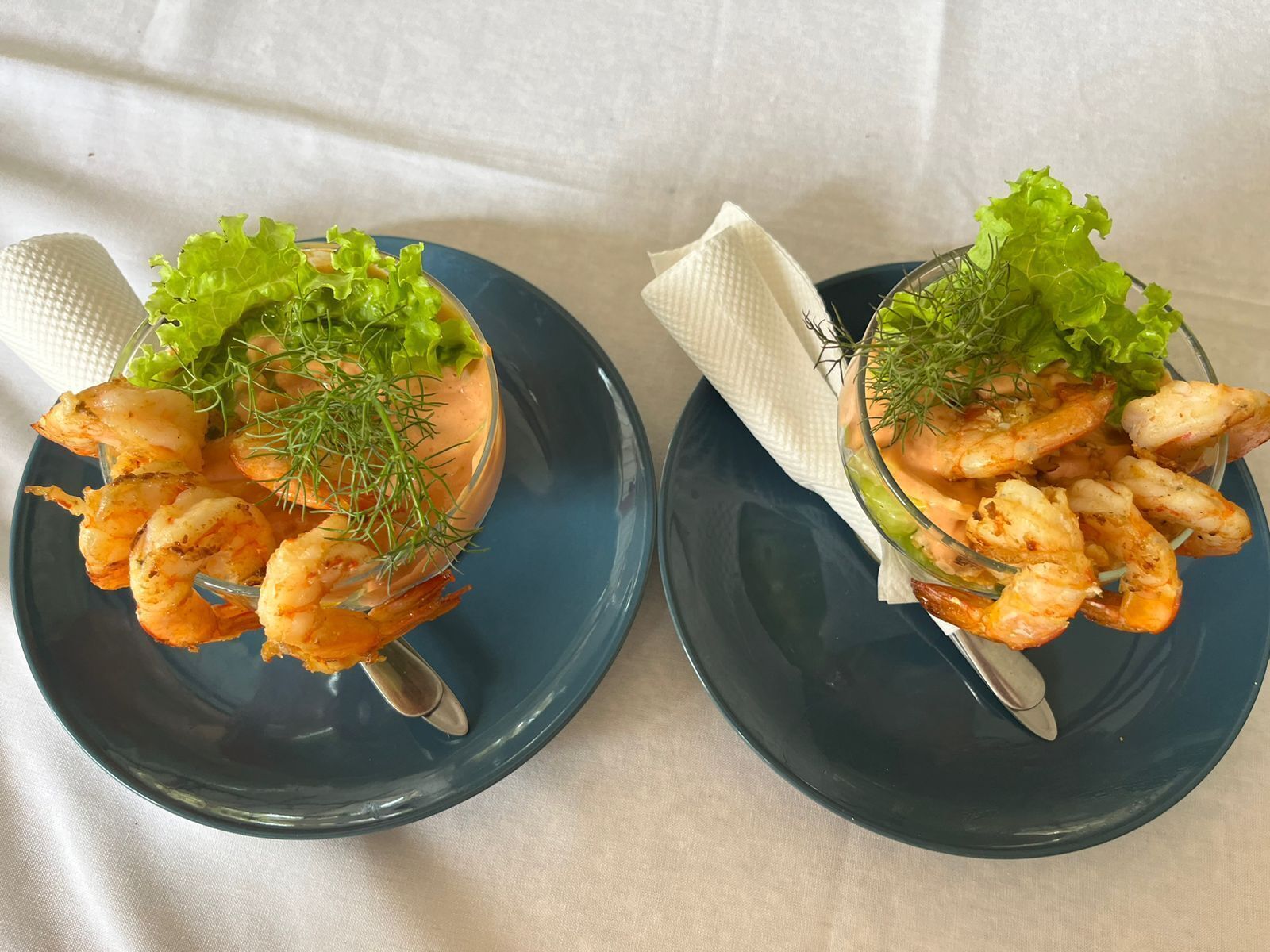 Two plates of shrimp with lettuce and dill on a table.